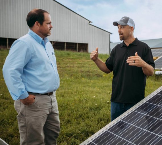 two men talking next to solar panel